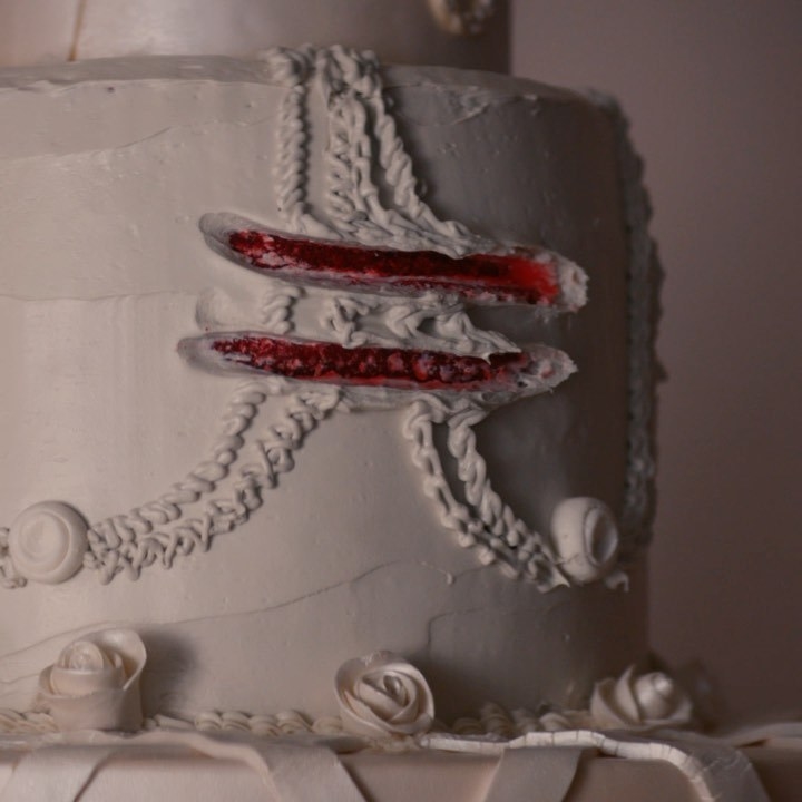 A closeup of a wedding cake, with two finger trails through the icing that show the red cake underneath