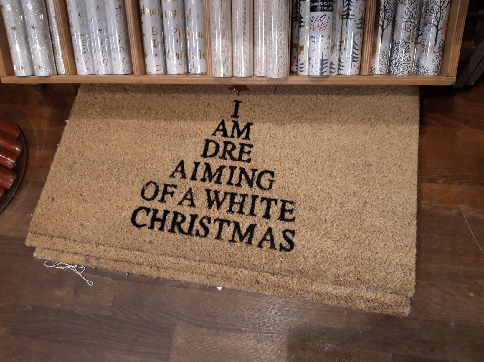 A doormat with the letters &quot;I / AM / DRE / AIMING / OF A WHITE / CHRISTMAS&quot; in the shape of a tree