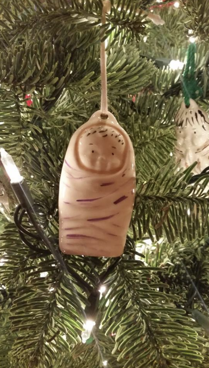 A baby Jesus ornament hanging on a tree and looking like half a thumb with a face on the nail bed