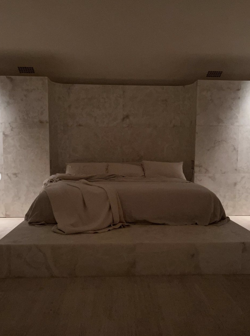A bed on a raised platform with seemingly marble walls surrounding it