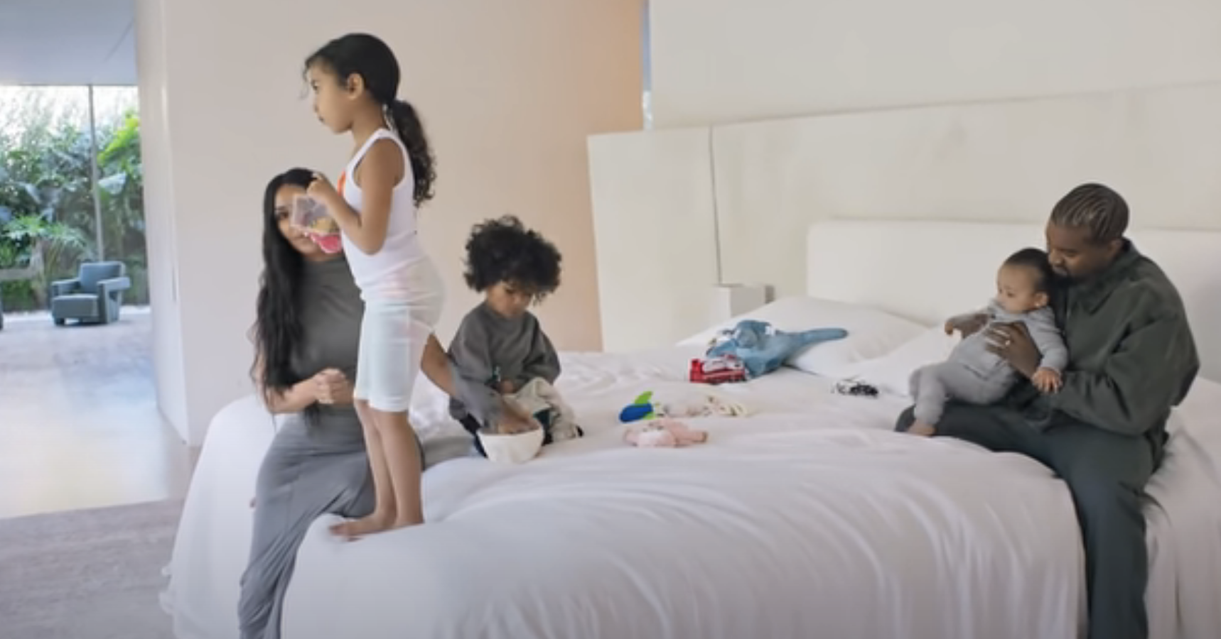 Kim sitting on a the bed with her kids and Kanye with the decor being much lighter and airy