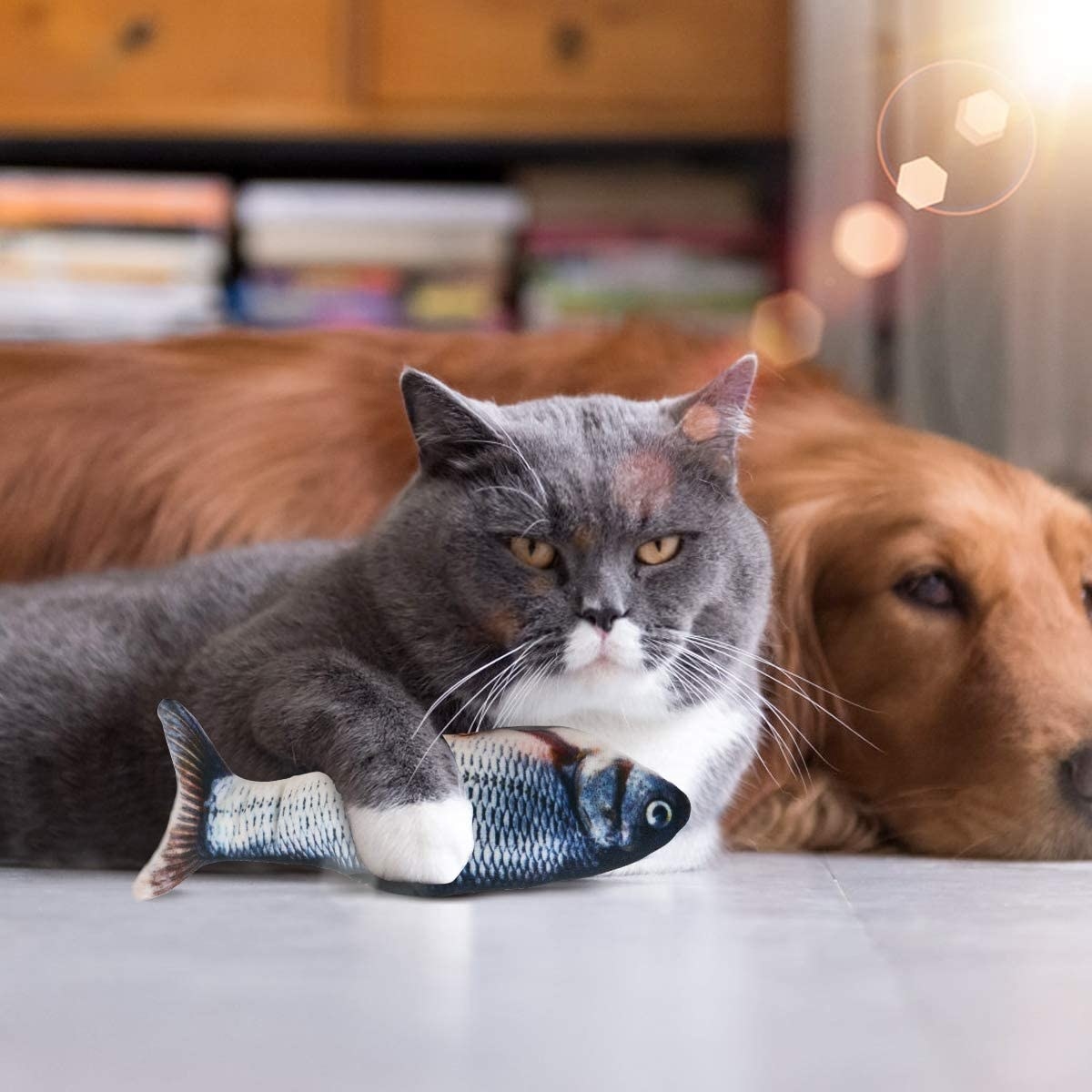 A cat holding the flopping fish while lying next to a dog