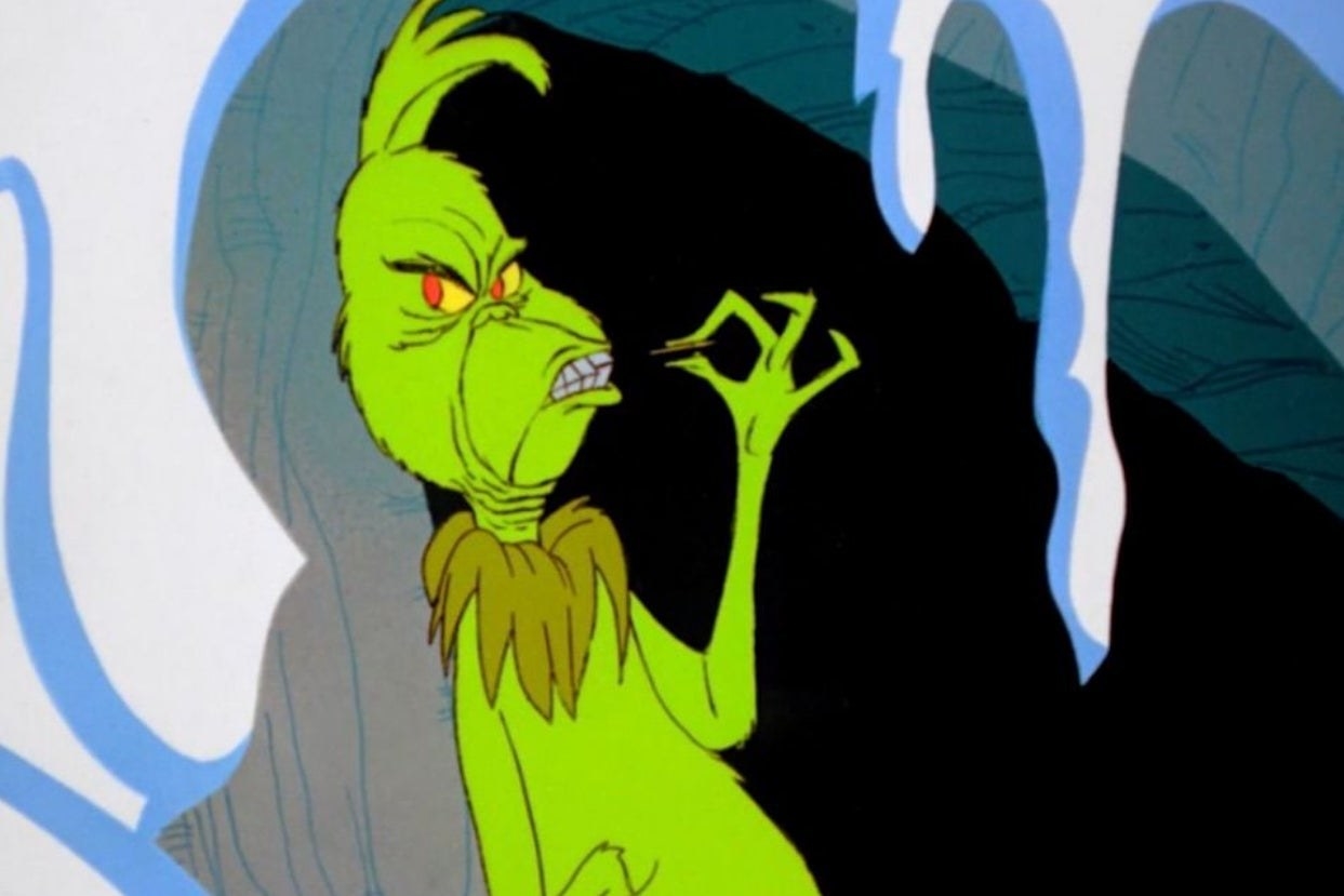 The animated Grinch biting down on a toothpick while leaning against the entry of an icy cave