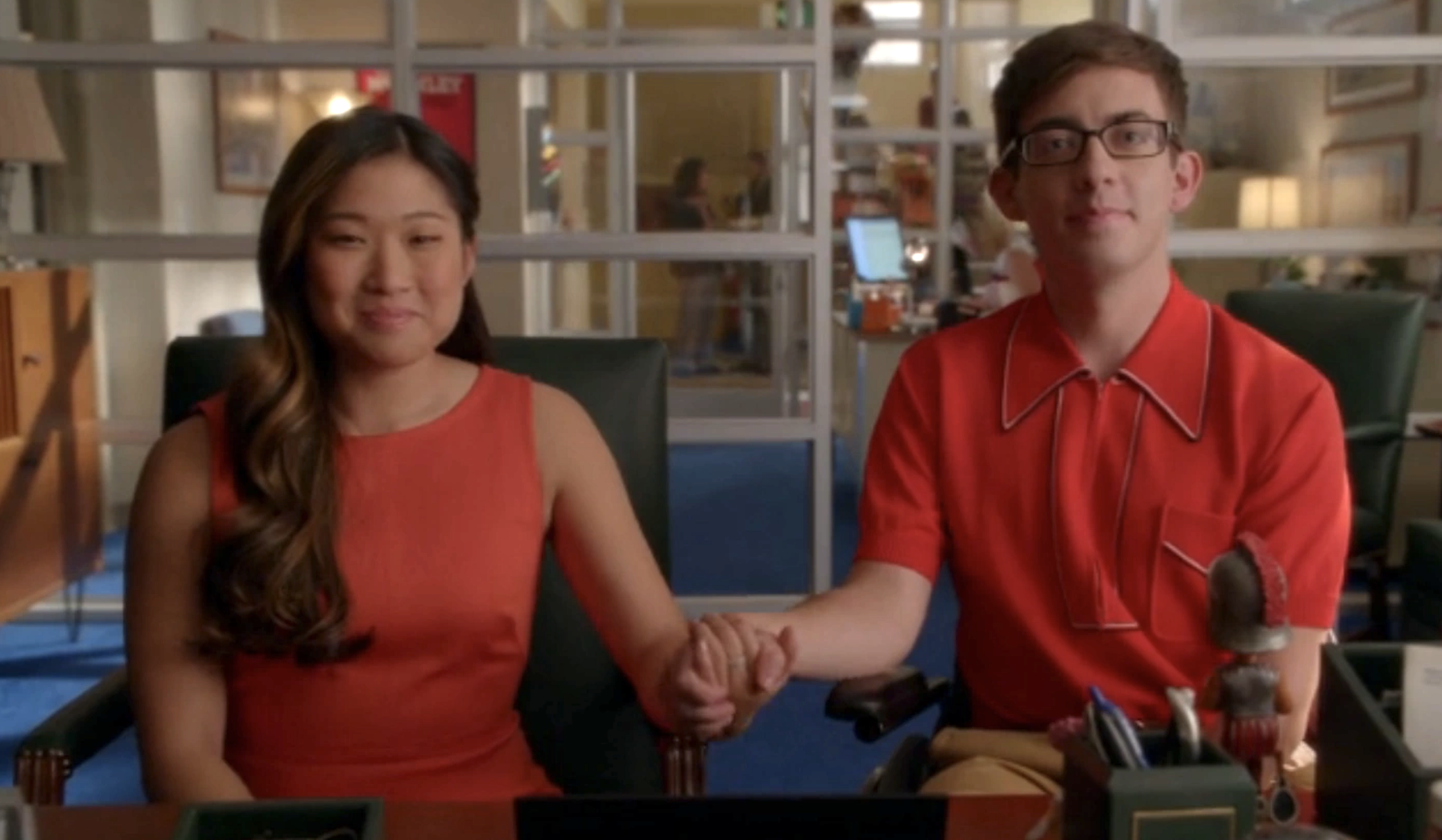 Tina and Artie sitting in a school office holding hands
