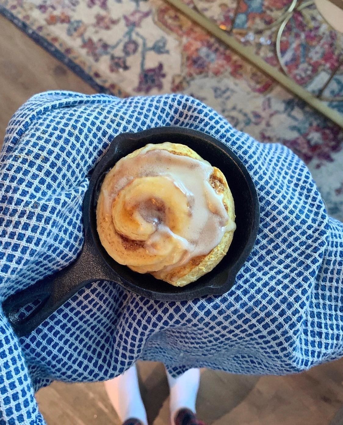 a cast iron skillet with a single cinnamon roll in it