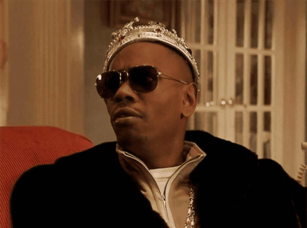 Dave Chappelle wearing a crown and sunglasses and hugging cash