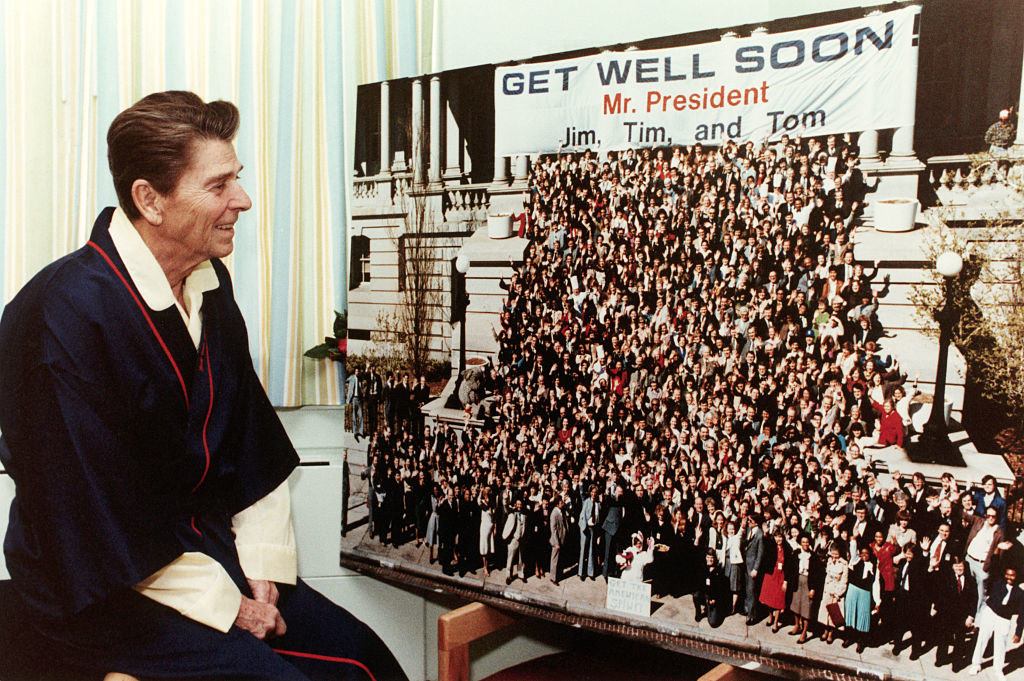 Reagan looking at people and a sign that says, &quot;Get well soon, Mr President&quot;