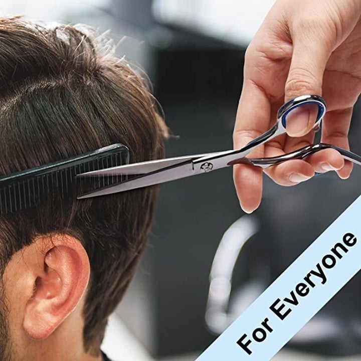 hand holds silver shears and comb while trimming short dark hair