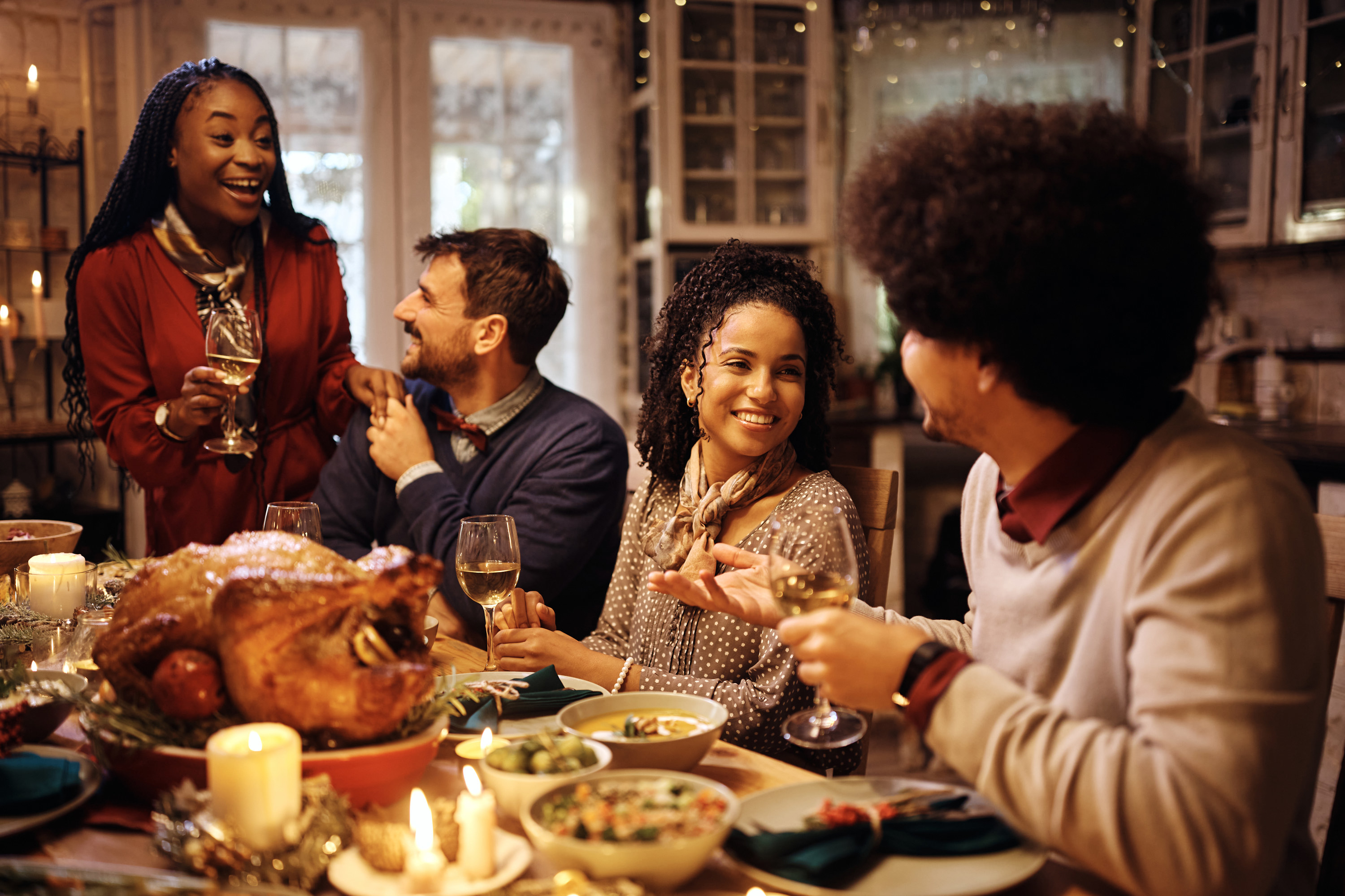 Happy African American woman enjoying in conversation with her friend while gathering for Thanksgiving at dining table