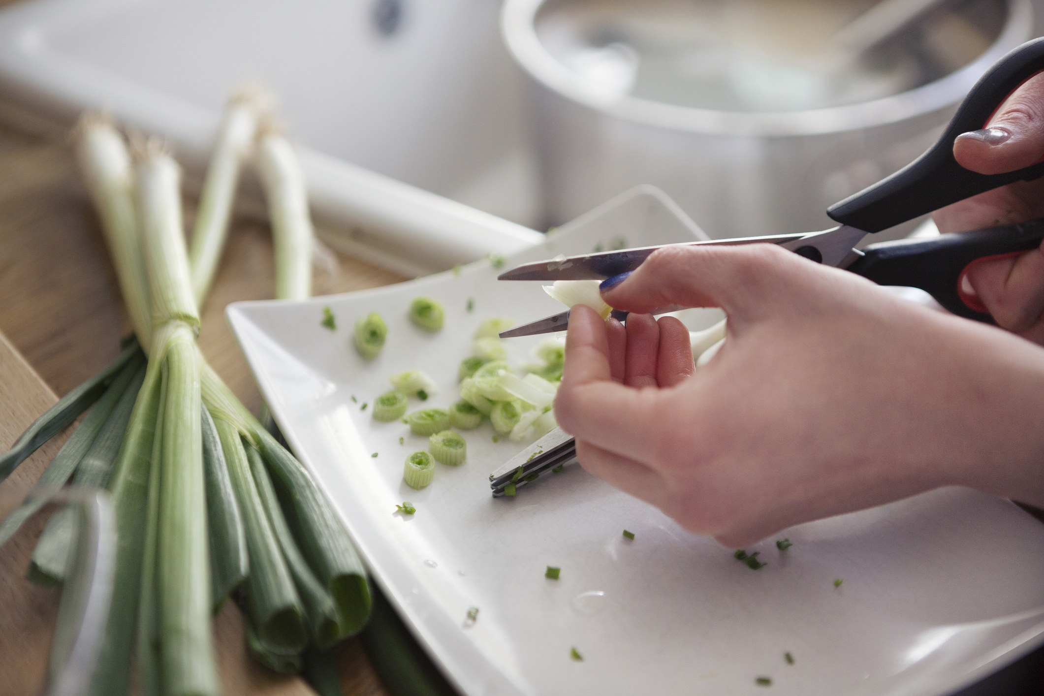 hands using scissors to cut up green onions