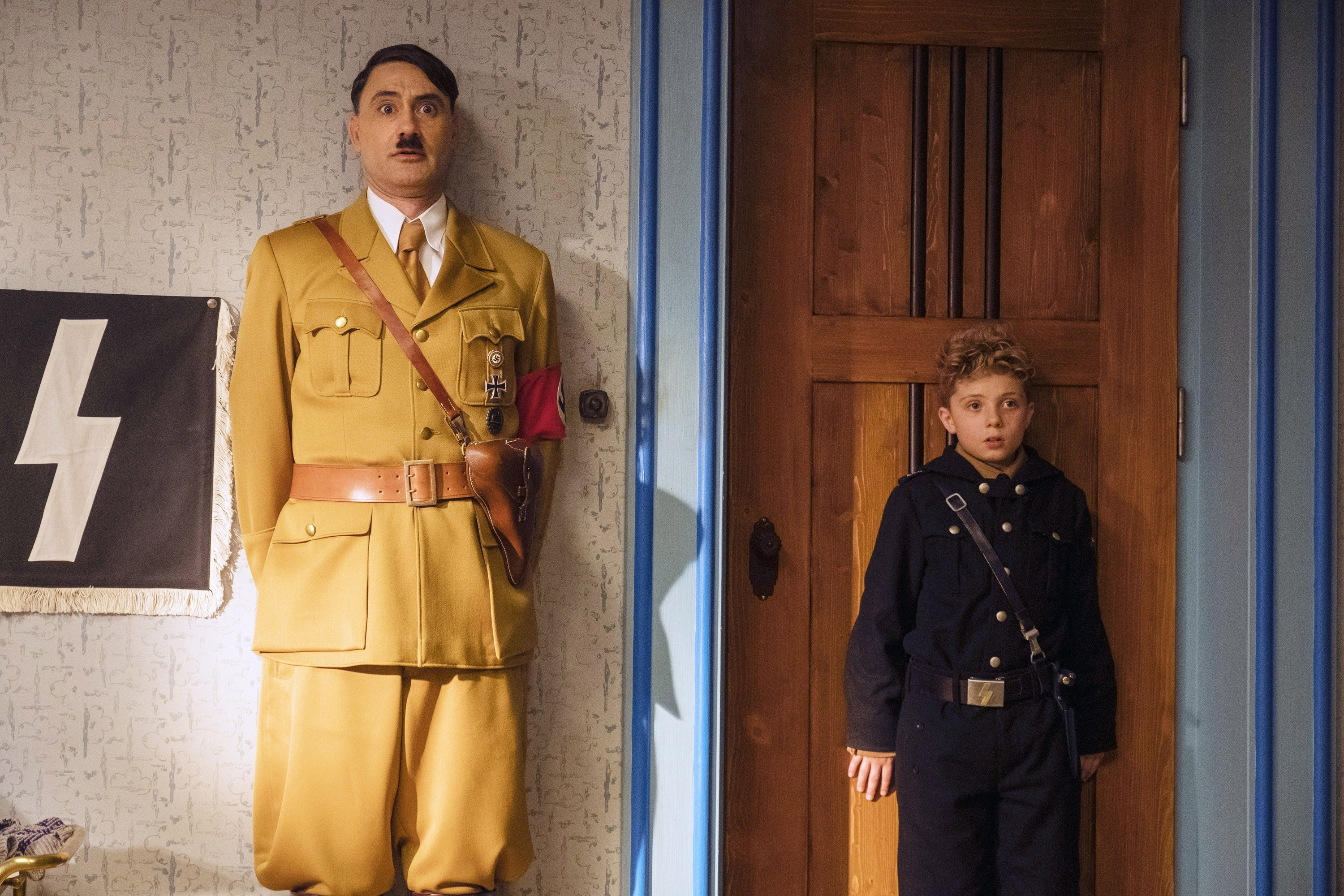 Taika Waititi and Roman Griffin Davis stand up against a wall together