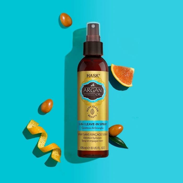A bottle of leave-in spray with a citrus peel, cut piece of citrus fruit, and argan seeds