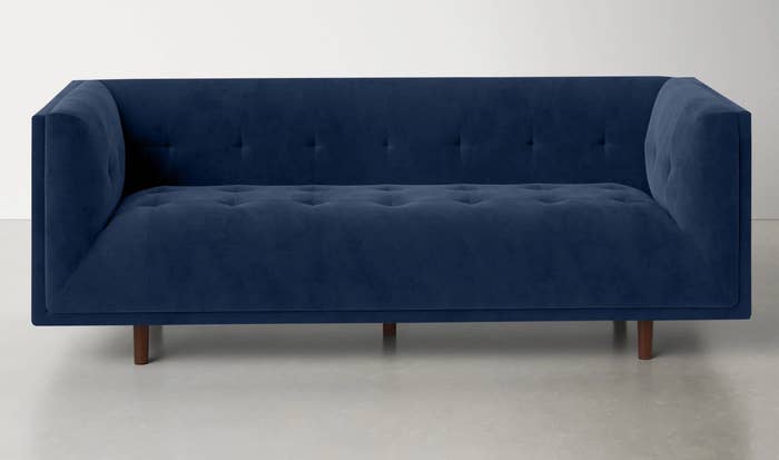 a sapphire velevet tufted and upholstered sofa with brown, wooden legs