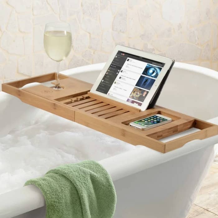 The light brown bathtub tray is holding an iPad, iPhone and a glass of wine