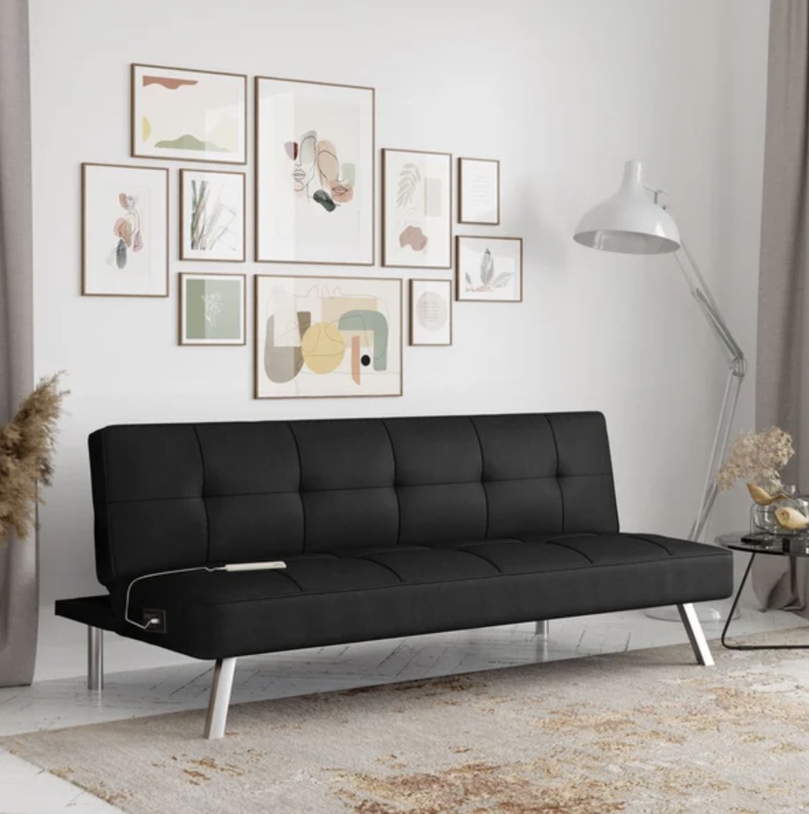 The black futon has silver legs and has a device plugged into its outlet