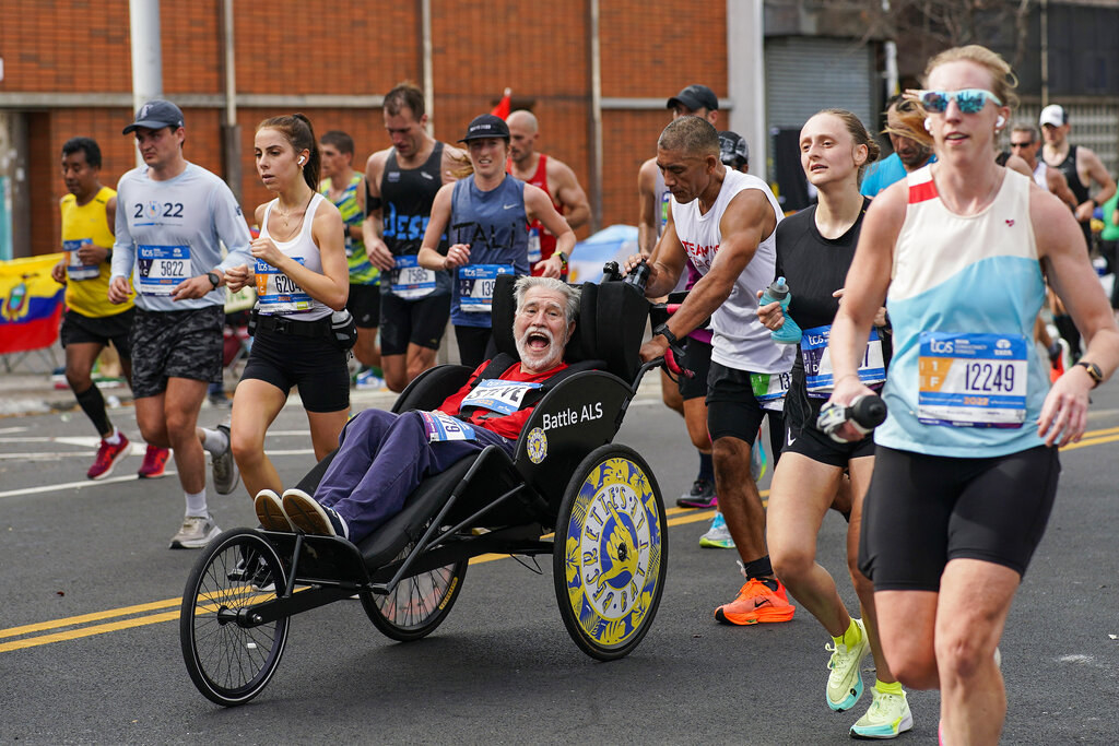 Runners and one pushing a man in a three-wheel chair