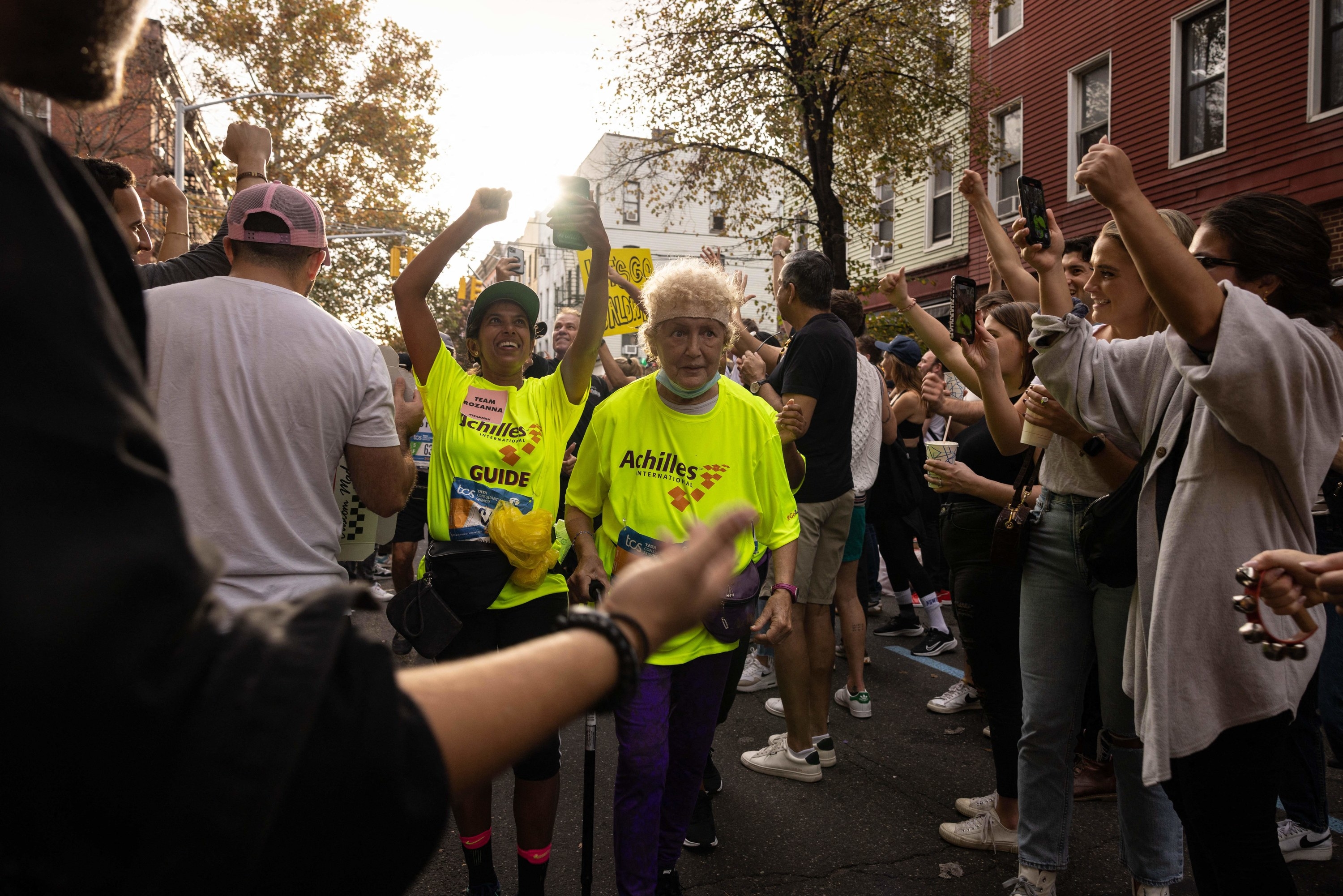 A crowded, narrow street with spectators and participants, including an older woman