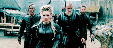 A woman viking leads a number of leather clad viking warriors through a village