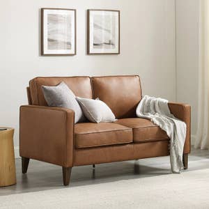 a brown faux leather loveseat with white throw pillows and a blanket on it