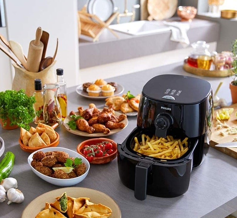 the black airfryer filled with french fries on a counter surrounded by other air-fried foods