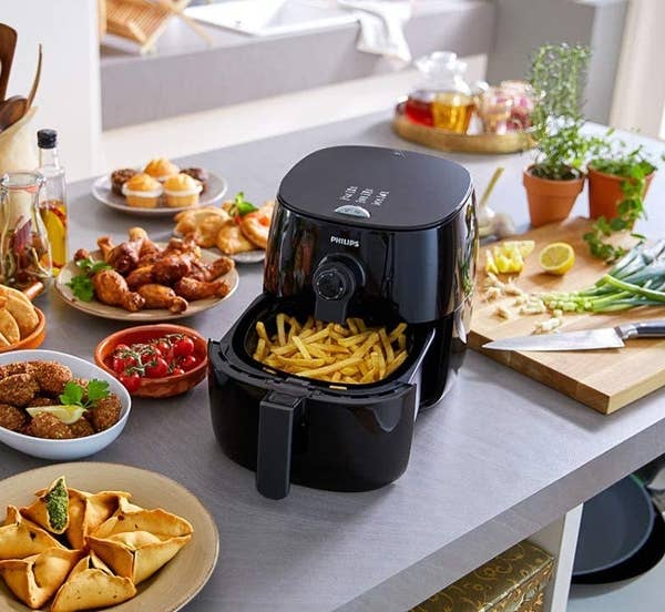 the black airfryer filled with french fries on a counter surrounded by other air-fried foods