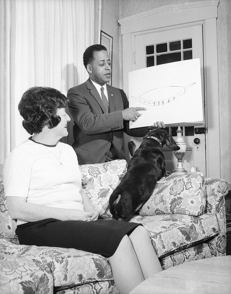 the husband showing off a drawing of the spaceship while the wife and dog are on the couch