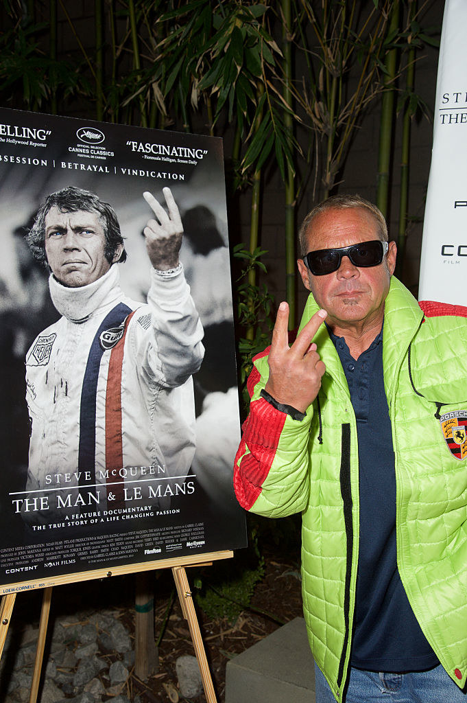 Chad in sunglasses and giving the peace sign next to a poster of Steve giving the same sign