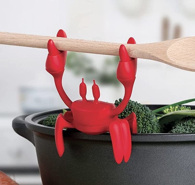 the crab on the edge of a pot holding a wooden spoon