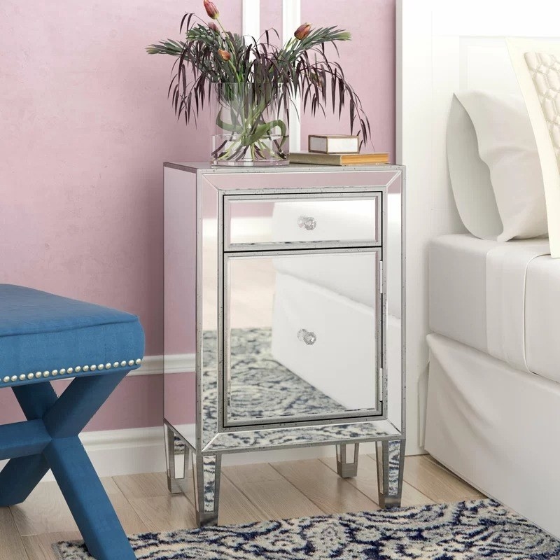 the silver mirror nightstand with plant vase on top next to a bed