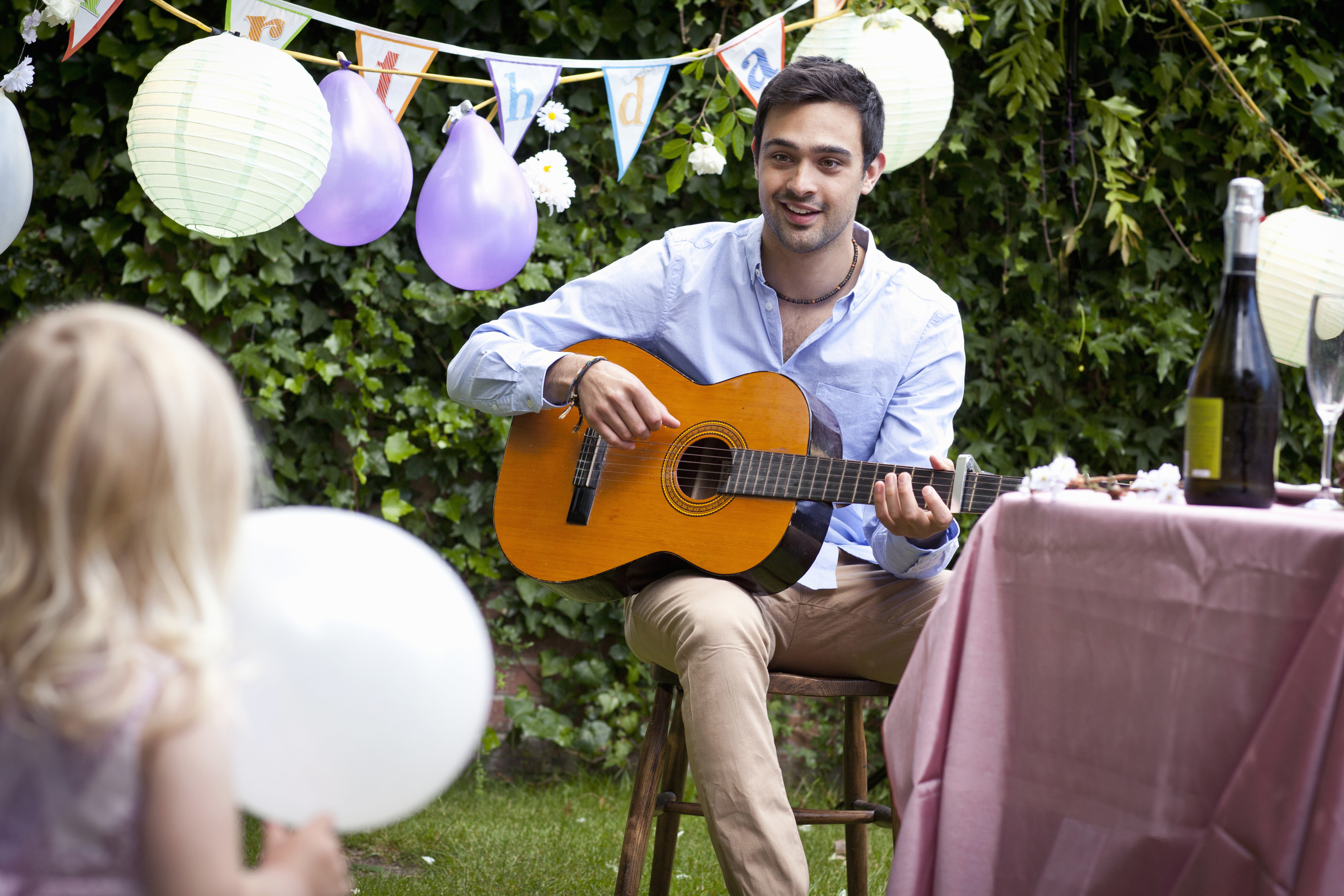 A performer plays guitar and sings at a child&#x27;s outdoor birthday party