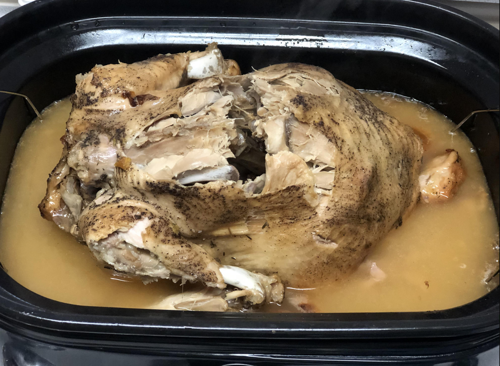 turkey with random pieces taken out of it sitting in a crockpot of juices
