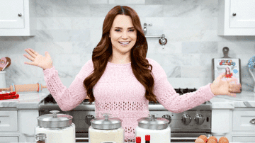 Rosanna Pansino standing in kitchen dancing with pink sweater on