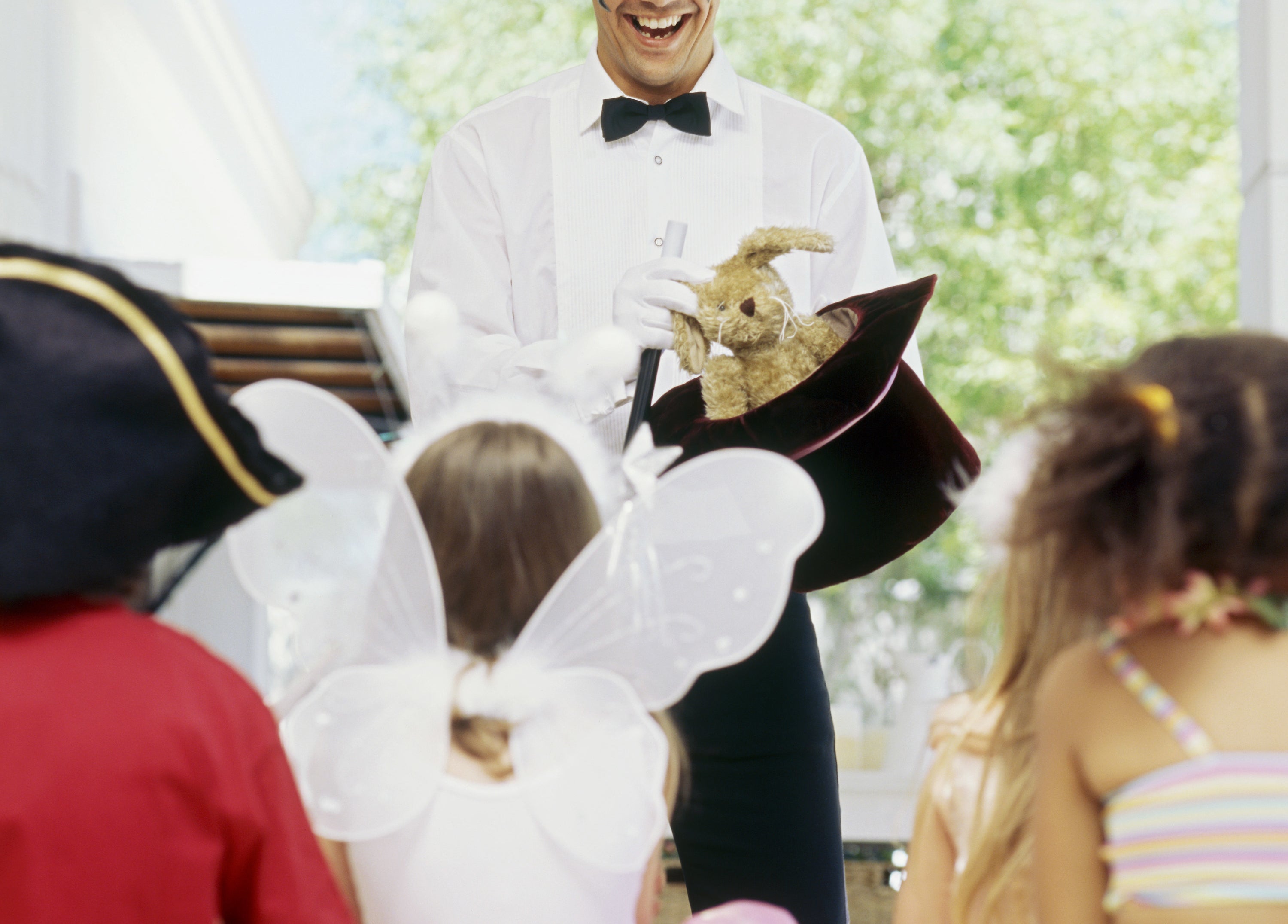 A magician at a kid&#x27;s costume party pulls a plush rabbit out of a hat