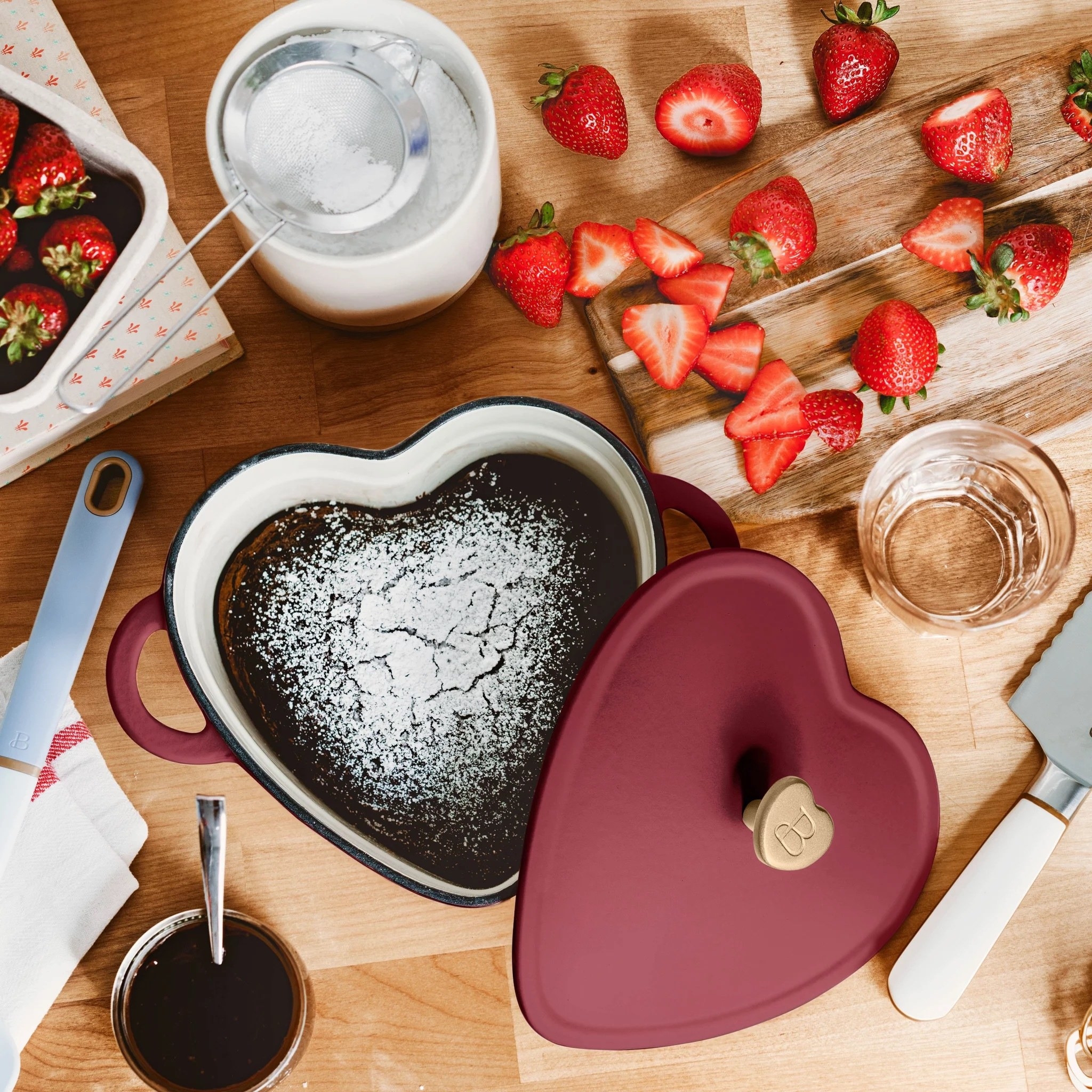 A red heart-sahped pot with brownies in it and kitchen utensils around it