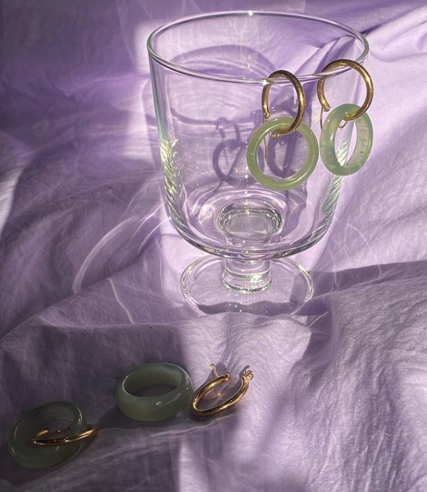 Glass cup on purple tablecloth with jade earrings hanging on.