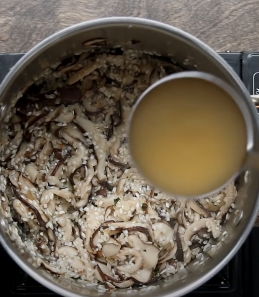 adding chicken stock to a pot of rice and sauteed mushrooms