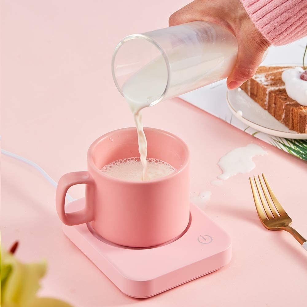 A person pouring milk into a mug on the warmer
