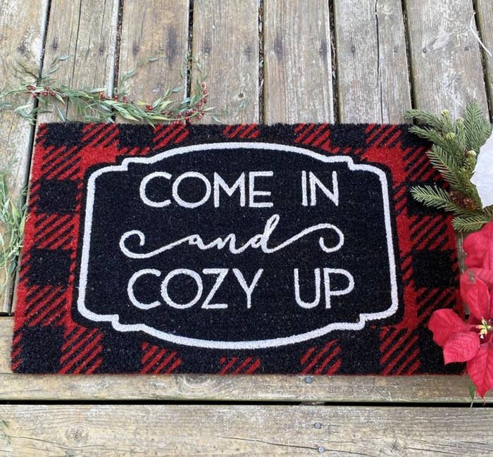 the checkered red and black welcome mat which reads &quot; come in and cozy up&quot; in white lettering