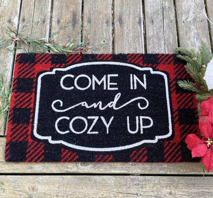 the checkered red and black welcome mat which reads " come in and cozy up" in white lettering