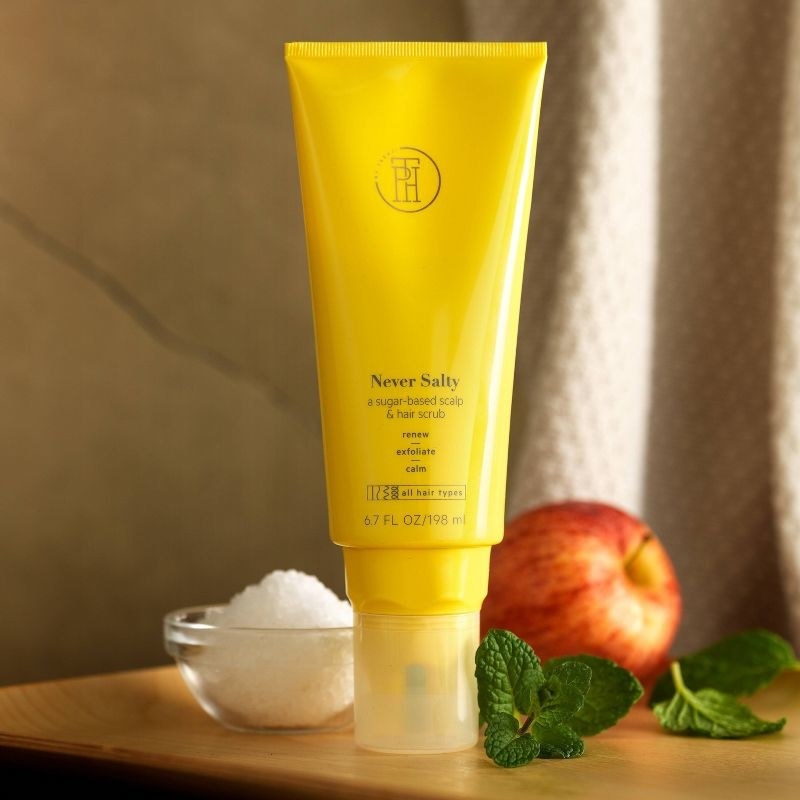 A tube of scalp scrub with an apple, sugar, and peppermint leaves