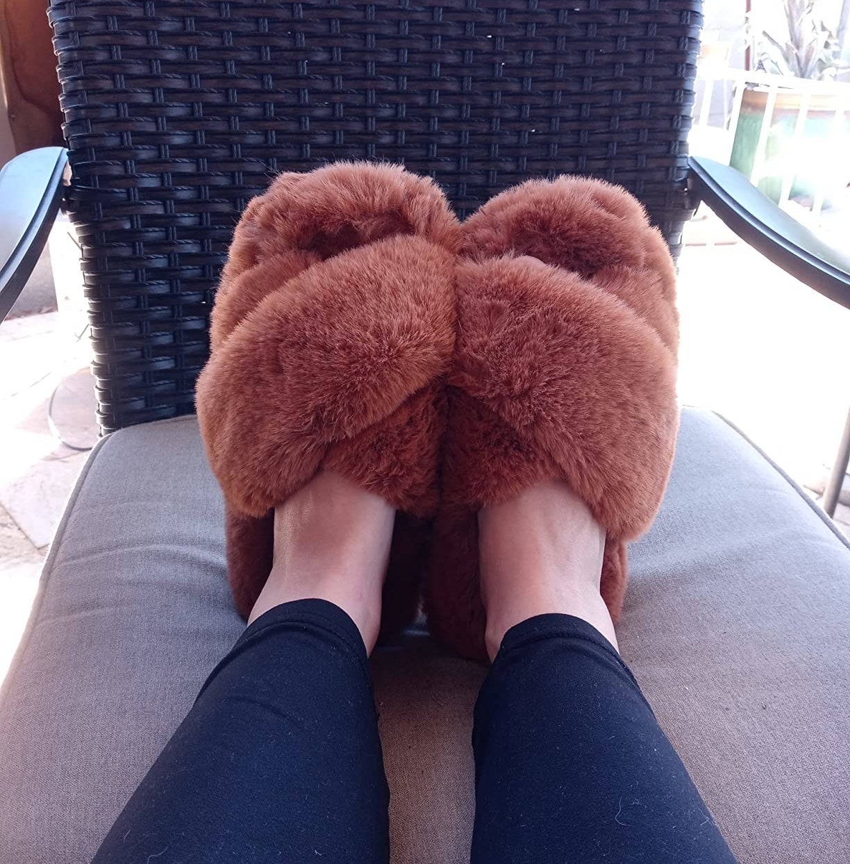 Reviewer with feet propped up on outdoor chair wearing the brown fluffy slippers