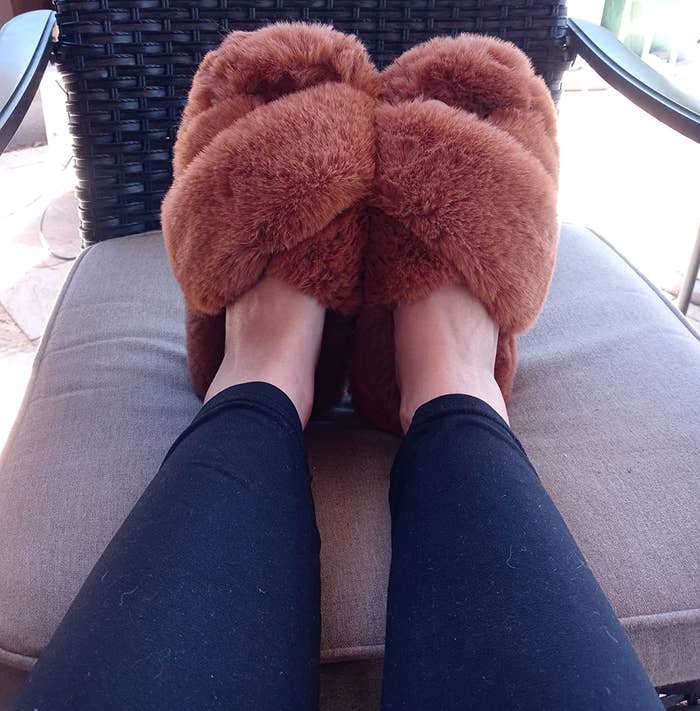 Reviewer with feet propped up on outdoor chair wearing the brown fluffy slippers