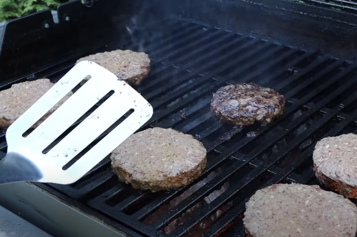 person grilling about to press on a burger cooking