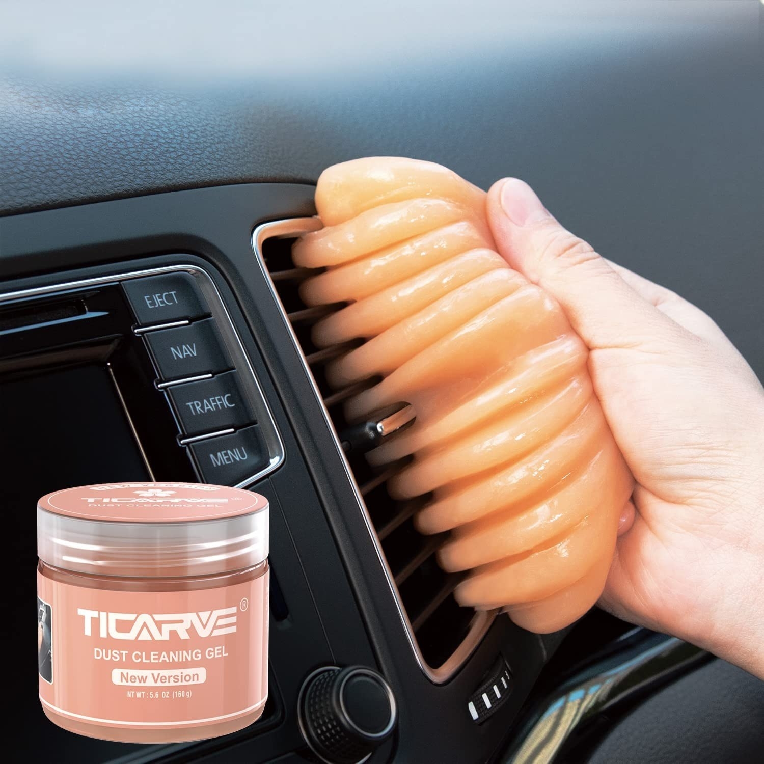 hand holds orange dust cleaning gel to clean between vents in car