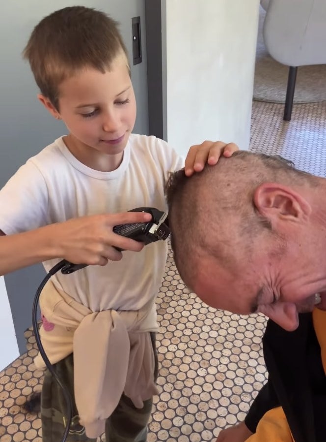 Robert bends his head over as his son takes a shaver to his head