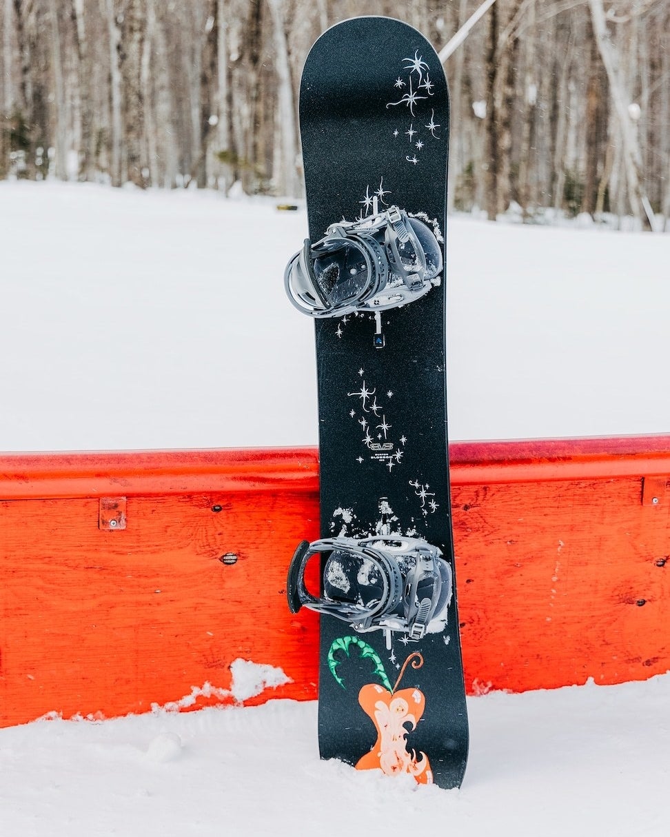 a snowboard leaning against a bright bench in the snow