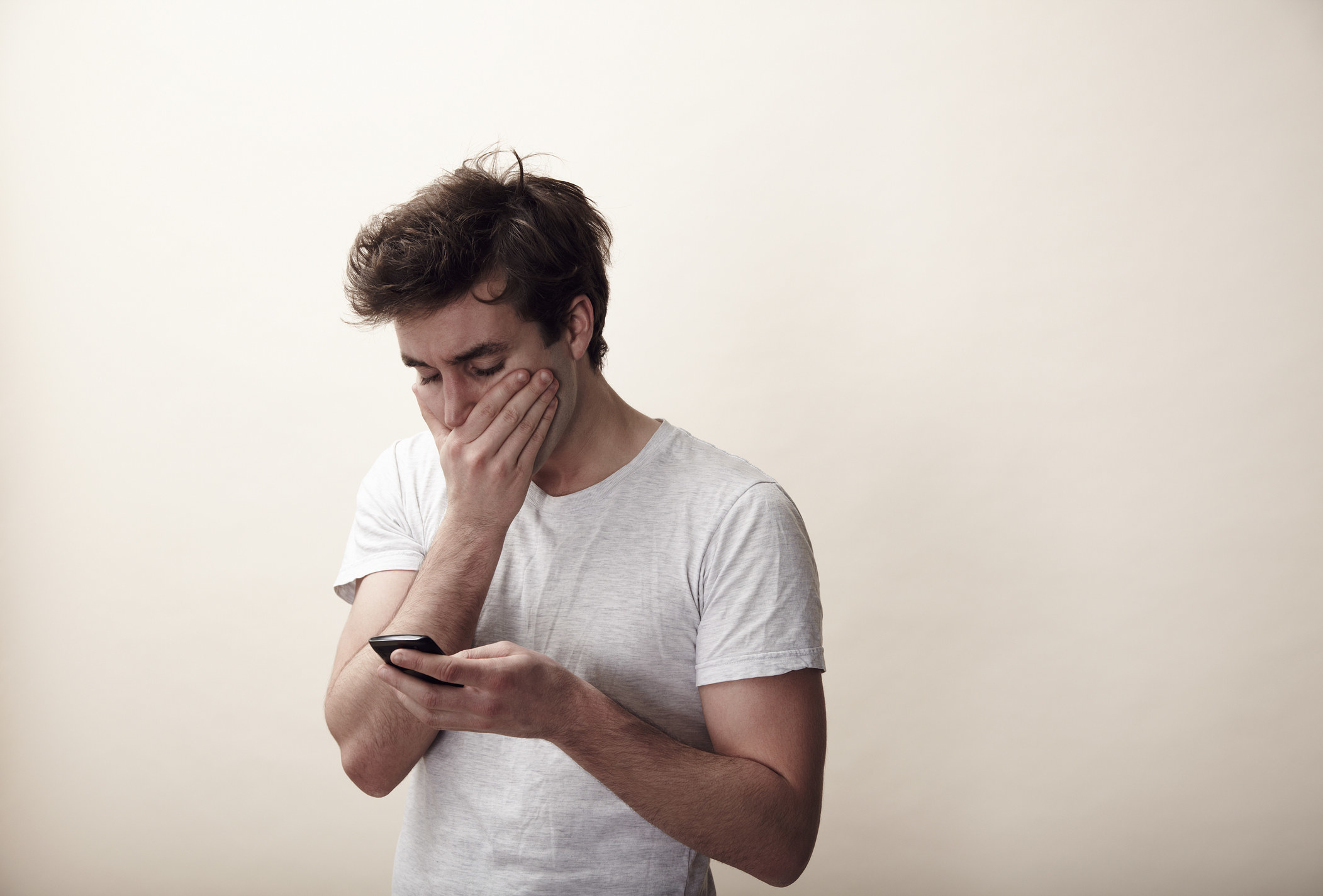 A man looking at his phone and covering his mouth in disbelief