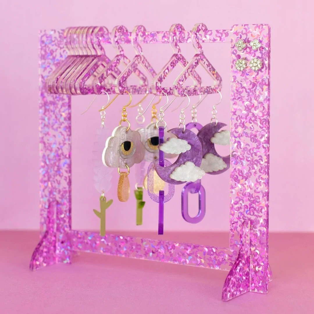 small glittery purple earring storage closet with matching hangers holding up colorful dangling earrings, including a pair with purple moons and clouds