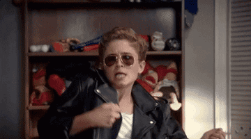 GIF of actor playing air guitar in a black leather jacket in &quot;The Goldbergs&quot;