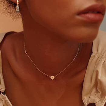 a model wearing a thin chain with a gold heart on it with an 'a' inside